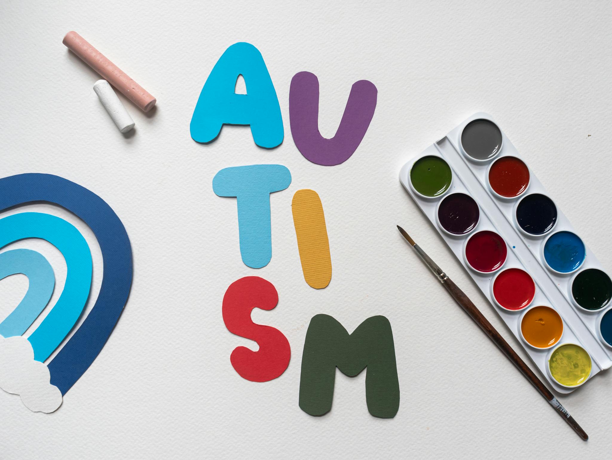 Colorful paper cutouts spelling 'AUTISM' with art supplies, emphasizing creativity and awareness.