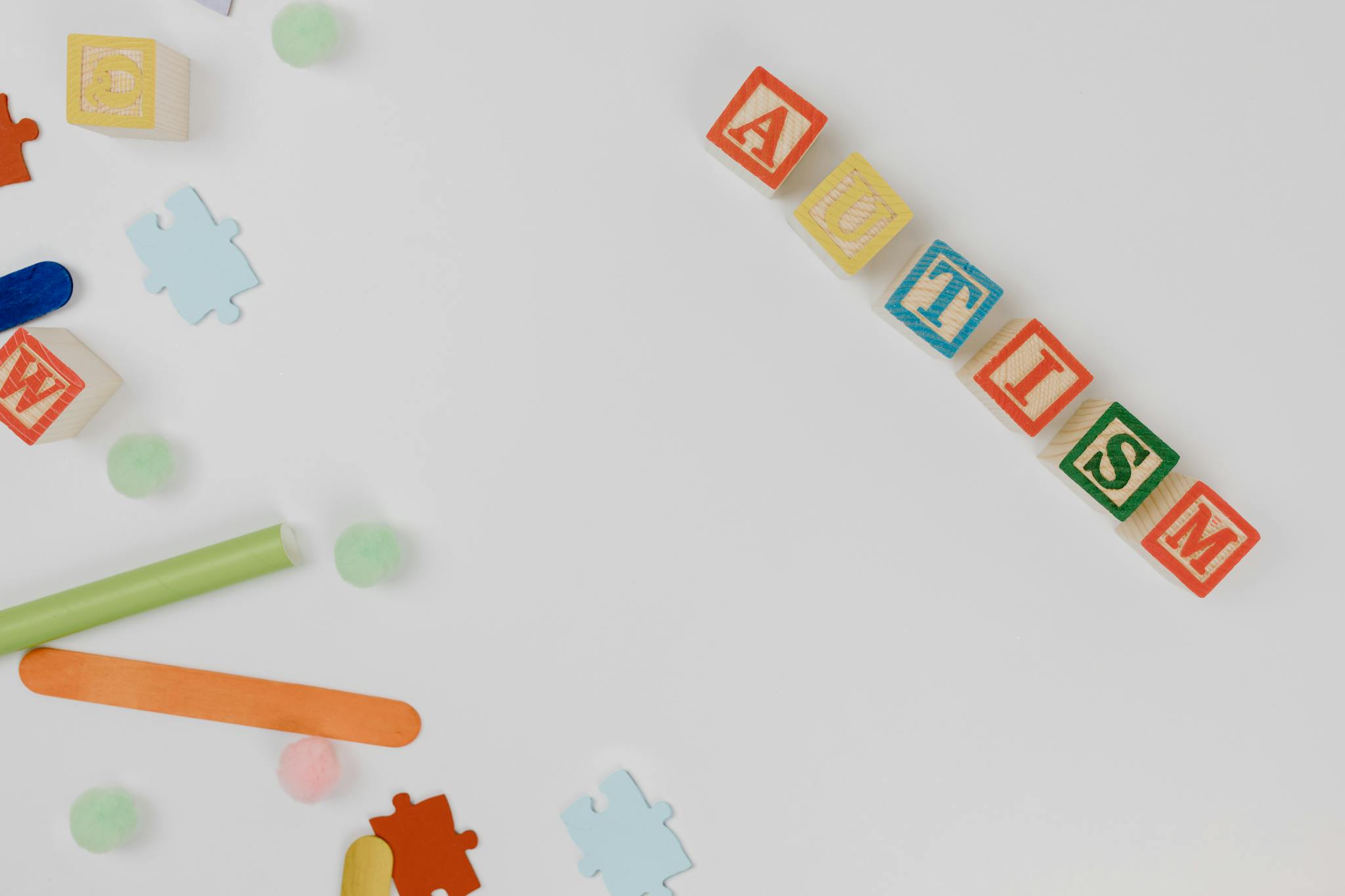 Top view of colorful wooden blocks spelling 'autism' surrounded by puzzle pieces symbolizing autism awareness.