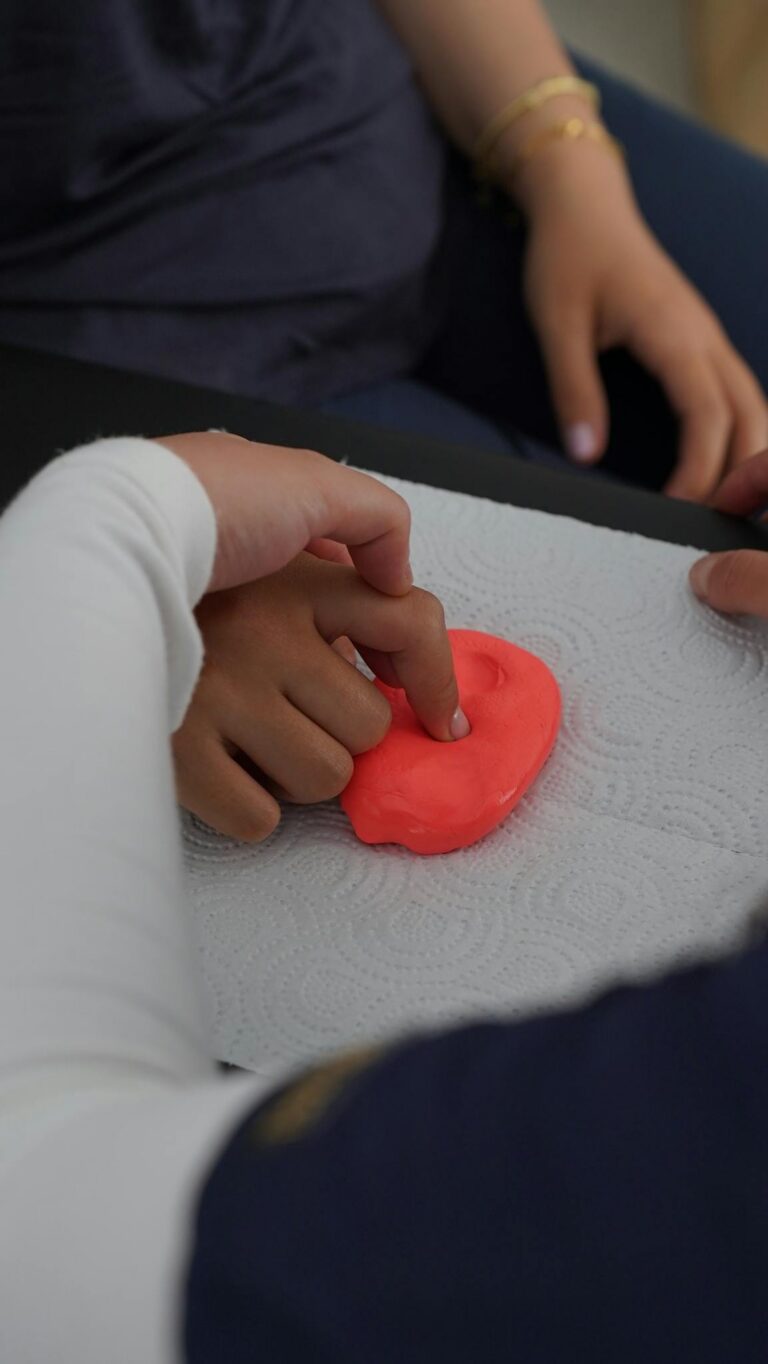 Close-up of hands manipulating putty during therapy session, emphasizing motor skills.