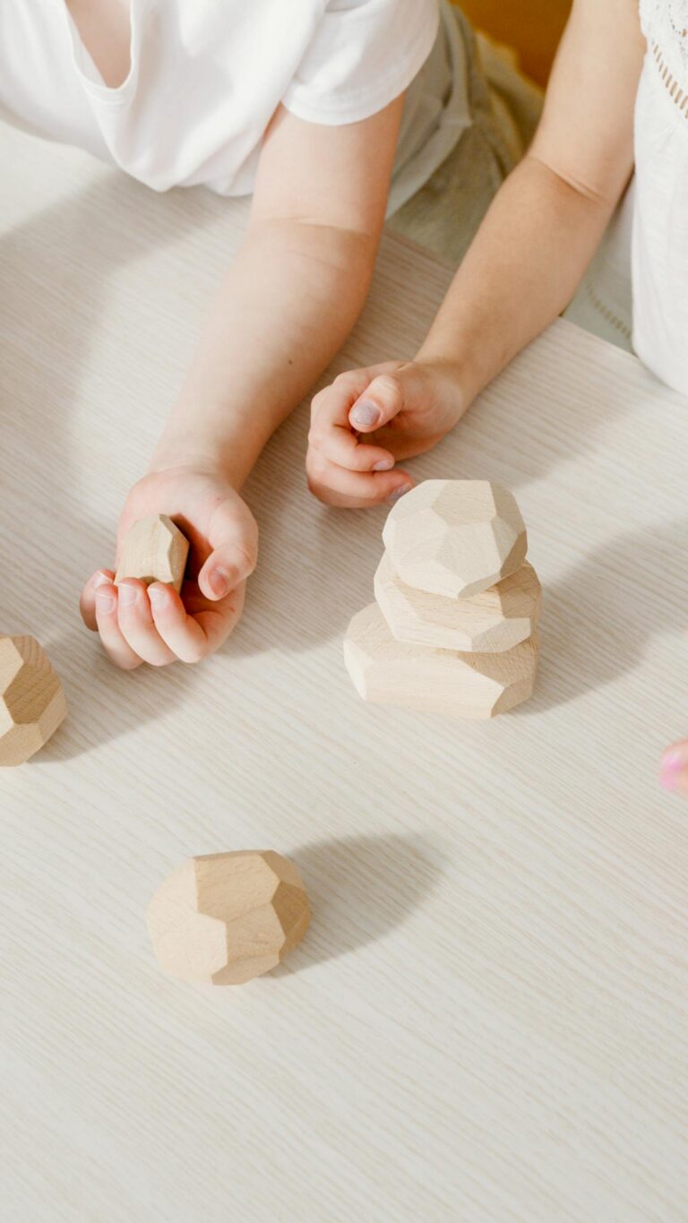 Close-up of kids' hands stacking geometric wooden blocks on a table.